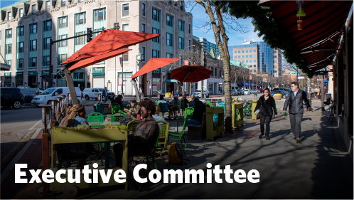 People dining outdoors with pedestrians walking by in the city