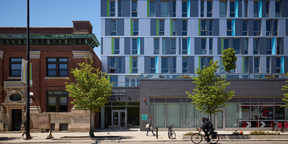 Low apartment building with pedestrian and bicycler in front.
